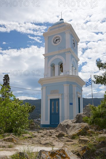 A blue and white clock tower under a sunny sky with the Greek flag and surrounding nature, Poros, Poros Island, Saronic Islands, Peloponnese, Greece, Europe