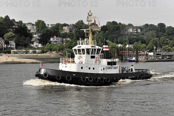 A tugboat sailing on a river (Elbe) with a city in the background, Hamburg, Hanseatic City of Hamburg, Germany, Europe