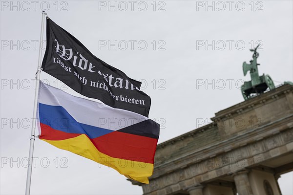 A waving flag with the inscription 'AeoeWiderstand laesst sich nicht verbieten'Aeo and a combination of German and Russian flags, with the Brandenburg Gate in the background, taken as part of the 'AeoeBauern-Proteste'Aeo in Berlin, 22 March 2024