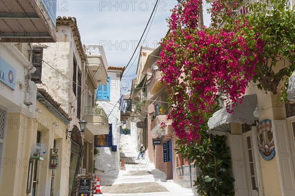Narrow alley in Mediterranean town with traditional houses and pink flowers under blue sky, Poros, Poros Island, Saronic Islands, Peloponnese, Greece, Europe