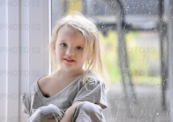 Little girl, 2-3 years, blonde, portrait, in front of window, rain, raindrops on window pane, smiling, Stuttgart, Baden-Wuerttemberg, Germany, Europe