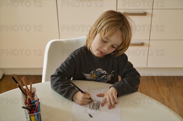 Indoor photo, boy, 4-5 years, blond, drawing on sheet of paper, pencils, table, straining, playing with tongue, Stuttgart, Baden-Wuerttemberg, Germany, Europe