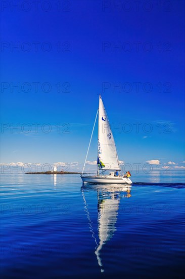 German sailboat sailing in an archipelago with water reflection in the sea and a lighthouse on a cliff