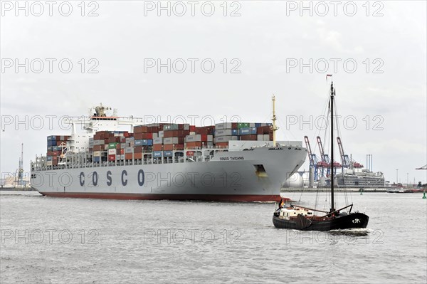 A large container ship next to a small sailing boat in a cloudy harbour, Hamburg, Hanseatic City of Hamburg, Germany, Europe
