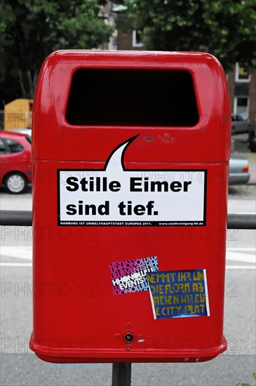 A bright red rubbish bin with stickers in front of a blurred city background, Hamburg, Hanseatic City of Hamburg, Germany, Europe