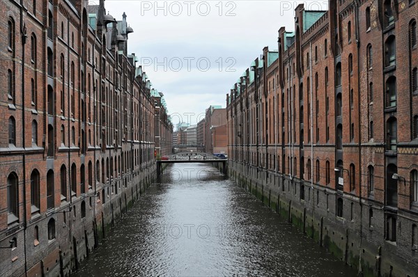 View of a quiet water canal surrounded by symmetrical brick buildings under a cloudy sky, Hamburg, Hanseatic City of Hamburg, Germany, Europe