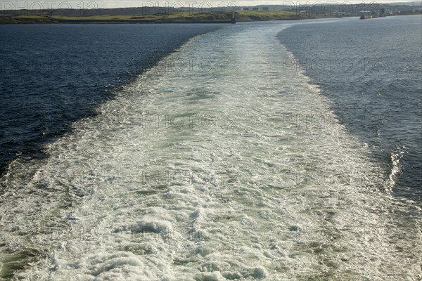 Large wake of ship at sea leaving land behind in the distance