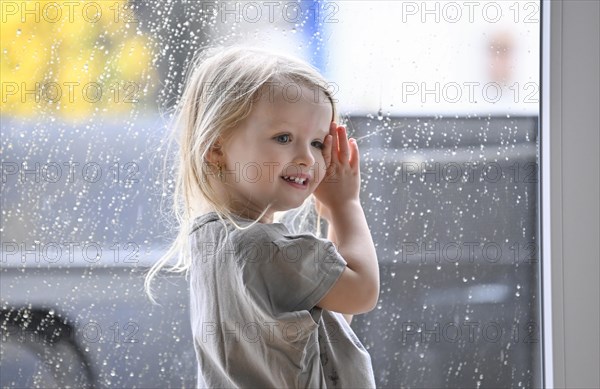 Little girl, 2-3 years, blonde, portrait, in front of window, rain, raindrops on window pane, smiling, Stuttgart, Baden-Wuerttemberg, Germany, Europe