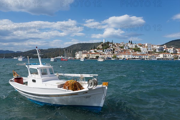 A fishing boat on the sea in front of a picturesque coastal town under a partly cloudy blue sky, view from Galatas, Argolis, to Poros, Poros Island, Saronic Islands, Peloponnese, Greece, Europe