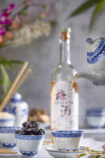Pouring tea, Asian tea set with blue patterns, a bottle of China plum wine in the background, dried fruit