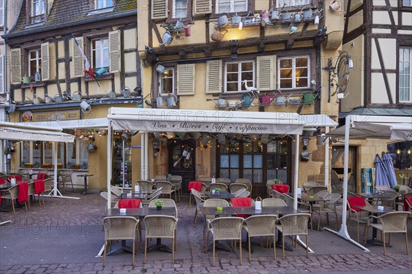 Catering establishments in historic half-timbered houses with watering cans decorating the facade and umbrellas, benches and tables outside in the old town centre of Colmar, Department Haut-Rhin, Grand Est, France, Europe