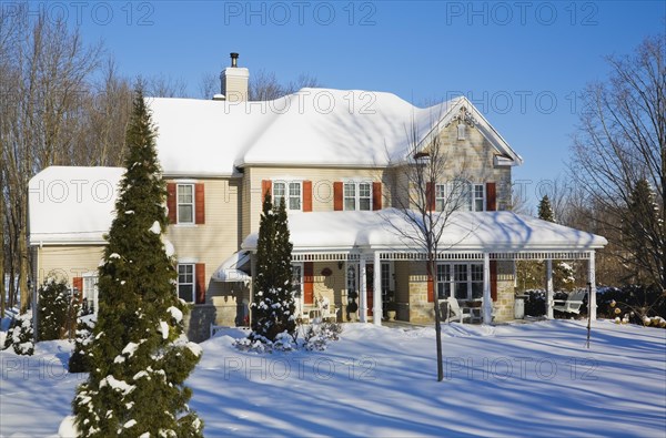 Two story beige vinyl siding with brownish red nuanced brick veneer and orange trim home in winter, Quebec, Canada, North America