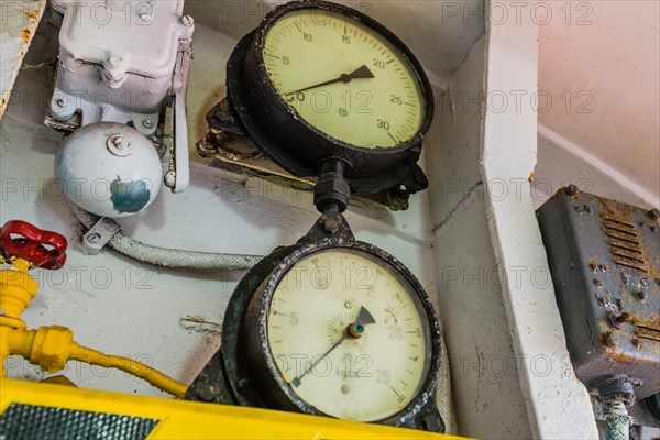 Old pressure gauges mounted above yellow and black striped ledge with valves and bell in background in Gangneung, South Korea, Asia