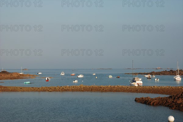 Calm seascape with moored boats, rock formations, and a clear blue sky