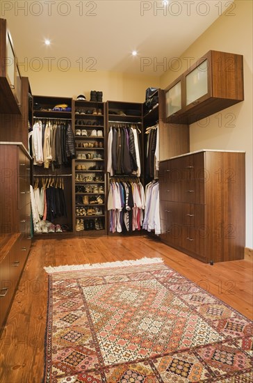 Walk-in closet with assorted men's and women's clothes and carpet in extension inside luxurious log cabin home, Quebec, Canada, North America