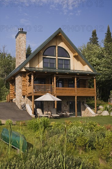 Handcrafted two story spruce log home cabin with fieldstone chimney, green sheet metal roof and green canoe in summer, Quebec, Canada, North America