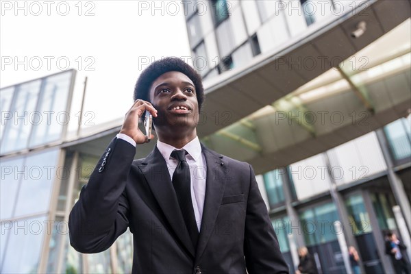 Low angle view close-up portrait of an elegant African young businessman working using phone outside a financial building