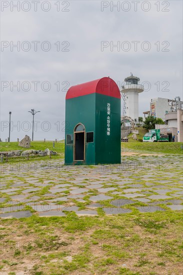 Green post box in a field with a lighthouse in the background under a cloudy sky, in Ulsan, South Korea, Asia