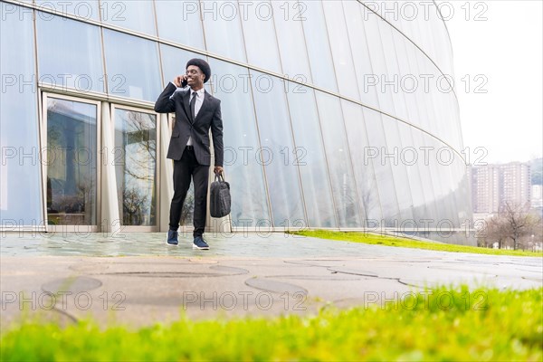 African businessman talking to the mobile holding computer bag in the street in a financial district