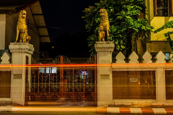 Long exposure captures the light trails at a temple gate with guarding statues, in Chiang Mai, Thailand, Asia
