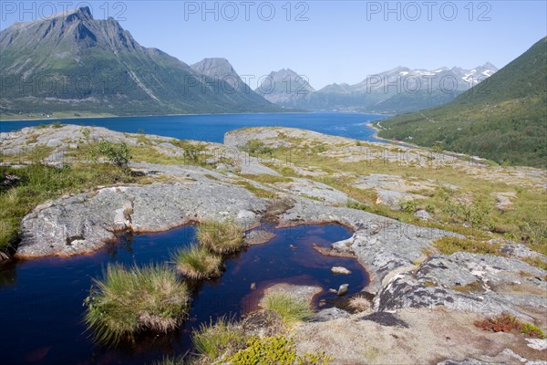 A tranquil landscape with a lake surrounded by mountains and rocks under a clear Lofoten Sea sky