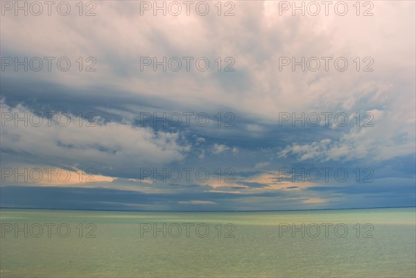 A serene seascape with a horizon dividing a cloudy sky and calm green-blue water