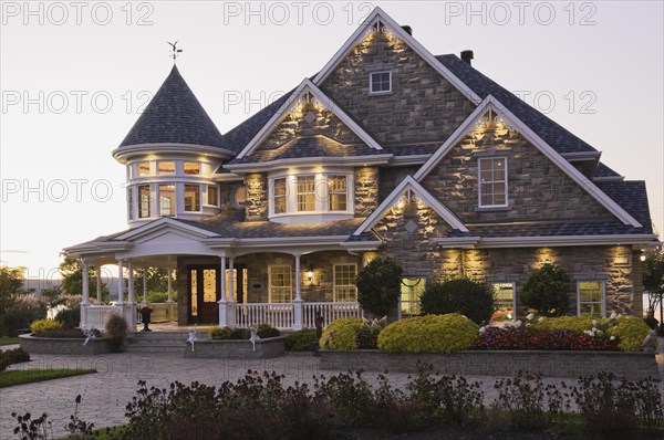 Elegant grey stone with white trim and blue asphalt shingles roof Victorian home facade at dusk in summer, Quebec, Canada, North America