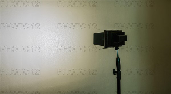 Continuous LED light mounted on tripod shinning on white patterned wall with deep shadows