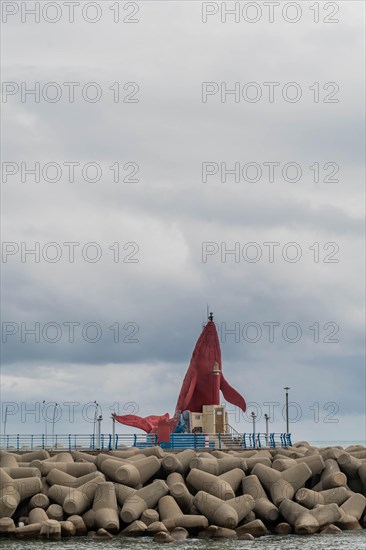 A red cloth flutters in the wind on a breaker with concrete blocks against a cloudy ocean backdrop, in Ulsan, South Korea, Asia