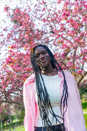 Vertical portrait of a beauty african woman smiling at camera next to flowering tree with pink flowers