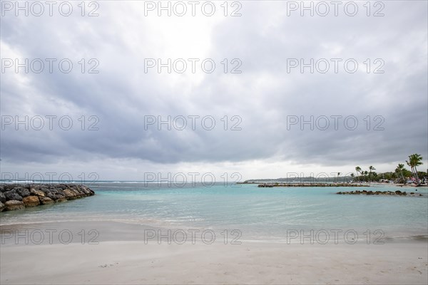 Caribbean dream beach with palm trees, white sandy beach and turquoise-coloured, crystal-clear water in the sea. Shallow bay on a cloudy day. Plage de Sainte Anne, Grande Terre, Guadeloupe, French Antilles, North America