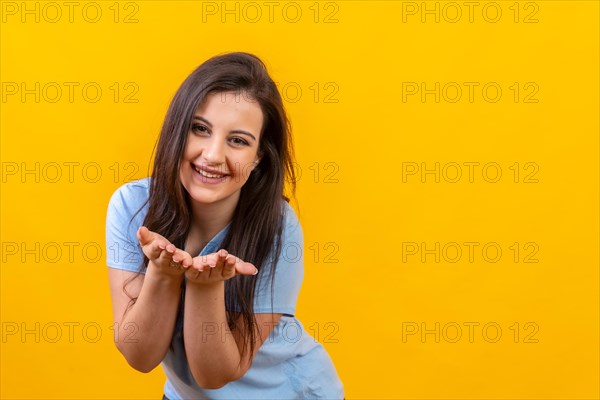 Studio portrait with yellow background of a smiling woman blowing a kiss with two hands