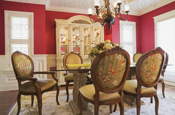 Glass top table with high-back wooden and upholstered chairs in dining room with buffet inside elegant style home, Quebec, Canada, North America