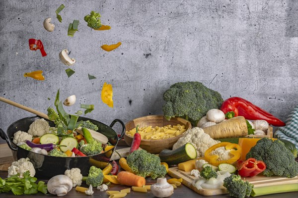 Pieces of vegetables floating in the air above a cooking pot, various fresh, partly cut vegetables next to it