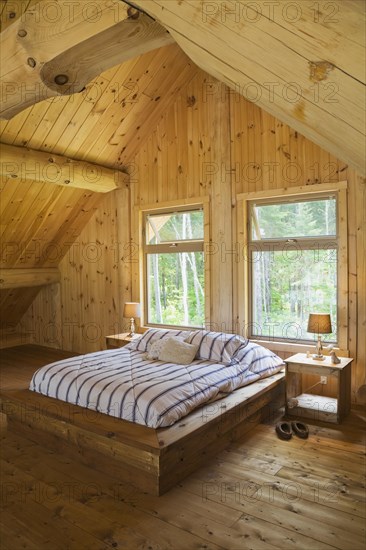 King size bed with wooden frame in master bedroom on upstairs floor inside handcrafted Eastern white pine Scandinavian log cabin home, Quebec, Canada, North America