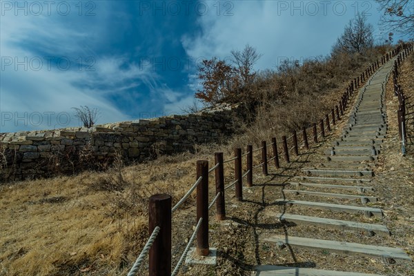 Wooden stairs up side of mountain next to section of mountain forest wall made of flat stones located near Boeun South Korea
