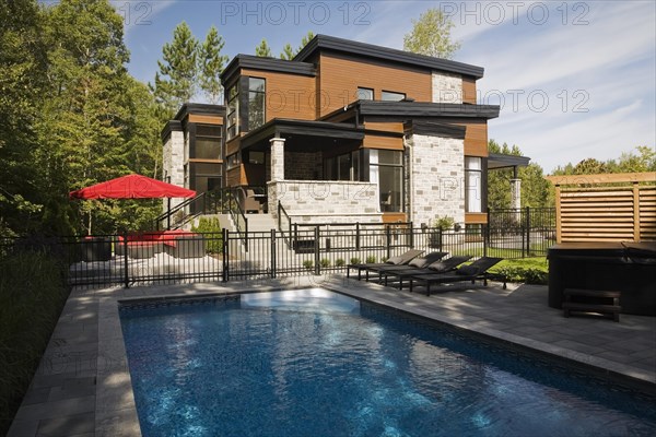 Two story grey, beige and tan cut stone with wood siding and black trim home and inground swimming pool in summer, Quebec, Canada, North America