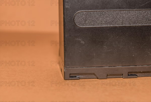 Closeup side view of used Lithium-ion battery on brown background. Selective focus on locking guides on bottom of battery