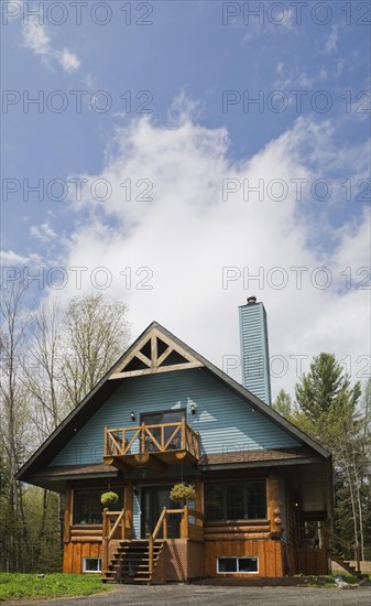 Post and beam cottage style hybrid log home facade with blue clapboard trim and timber elements in spring, Quebec, Canada. This image is property released. CUPR0266