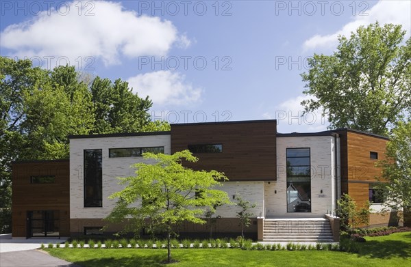 Beige stone with brown stained cedar wood modern cubist style residential home facade in spring, Quebec, Canada, North America