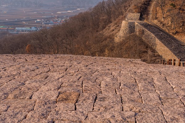 Section of mountain fortress wall made of flat stones located with rural community in background in Boeun, South Korea, Asia