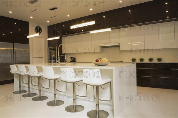 Quartz countertop island with white leather and stainless steel barsrools in spacious kitchen inside luxurious home, Quebec, Canada, North America