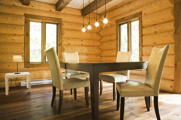 Brown wooden table and white cotton cloth upholstered high back chairs in dining room inside contemporary style log home, Quebec, Canada, North America