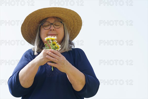 Smiling mature woman with white hair and hat with a bouquet of daisies in her hands isolated on a white background