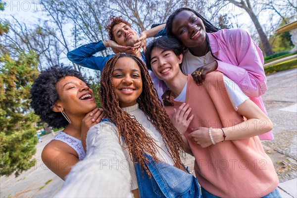 Personal perspective of five multi-ethnic young friends joking while taking a selfie in an urban park