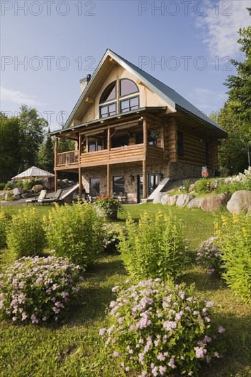 Handcrafted two story spruce log cabin home with fieldstone chimney and green sheet metal roof in summer, Quebec, Canada, North America