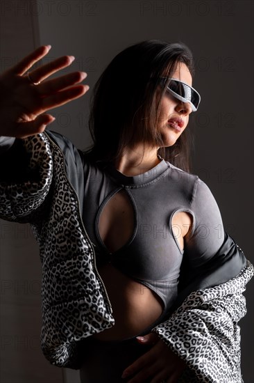 Studio portrait with grey background of a beauty woman gesturing using futuristic intelligent goggles