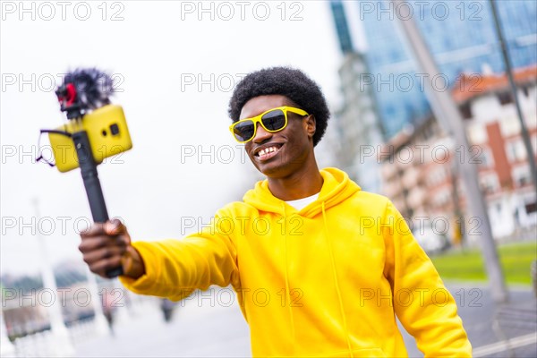 African young influencer broadcasting live in the city using a mobile attached on a tripod and microphone