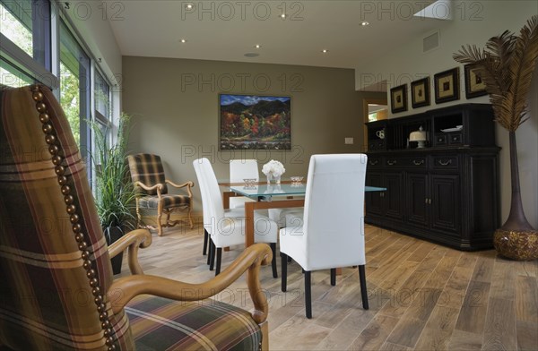 Clear glass top table and white leather high back chairs in dining room with beige ceramic tile floor inside modern cubist style home, Quebec, Canada, North America