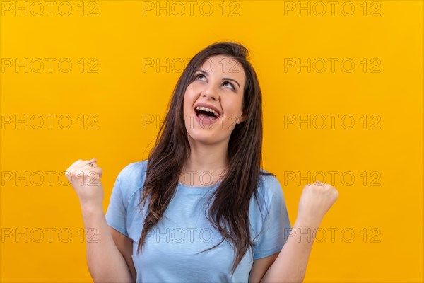 Studio portrait with yellow background of a woman looking up and raising fist celebrating